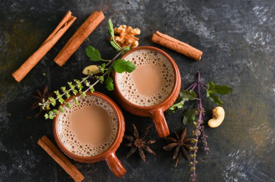 Top view of Indian Masala Chai or traditional beverage with tea, milk and spices Kerala India. Two cups of organic ayurvedic or herbal drink India, good in winter for immunity boosting.
